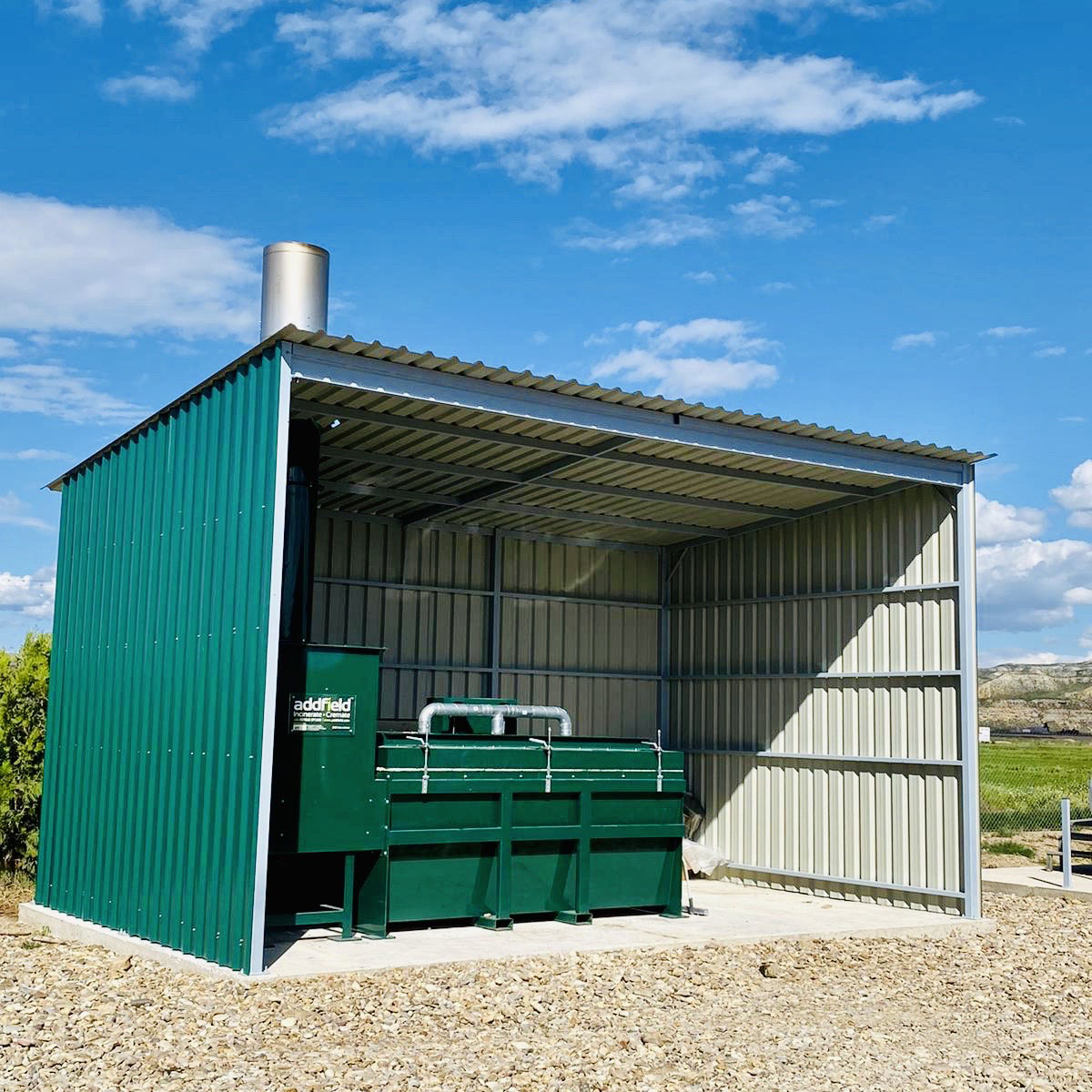 Green animal incinerator positioned inside a corrugated shelter