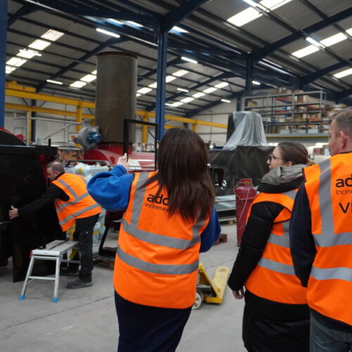 Four people in factory looking at incinerators with hi-vis